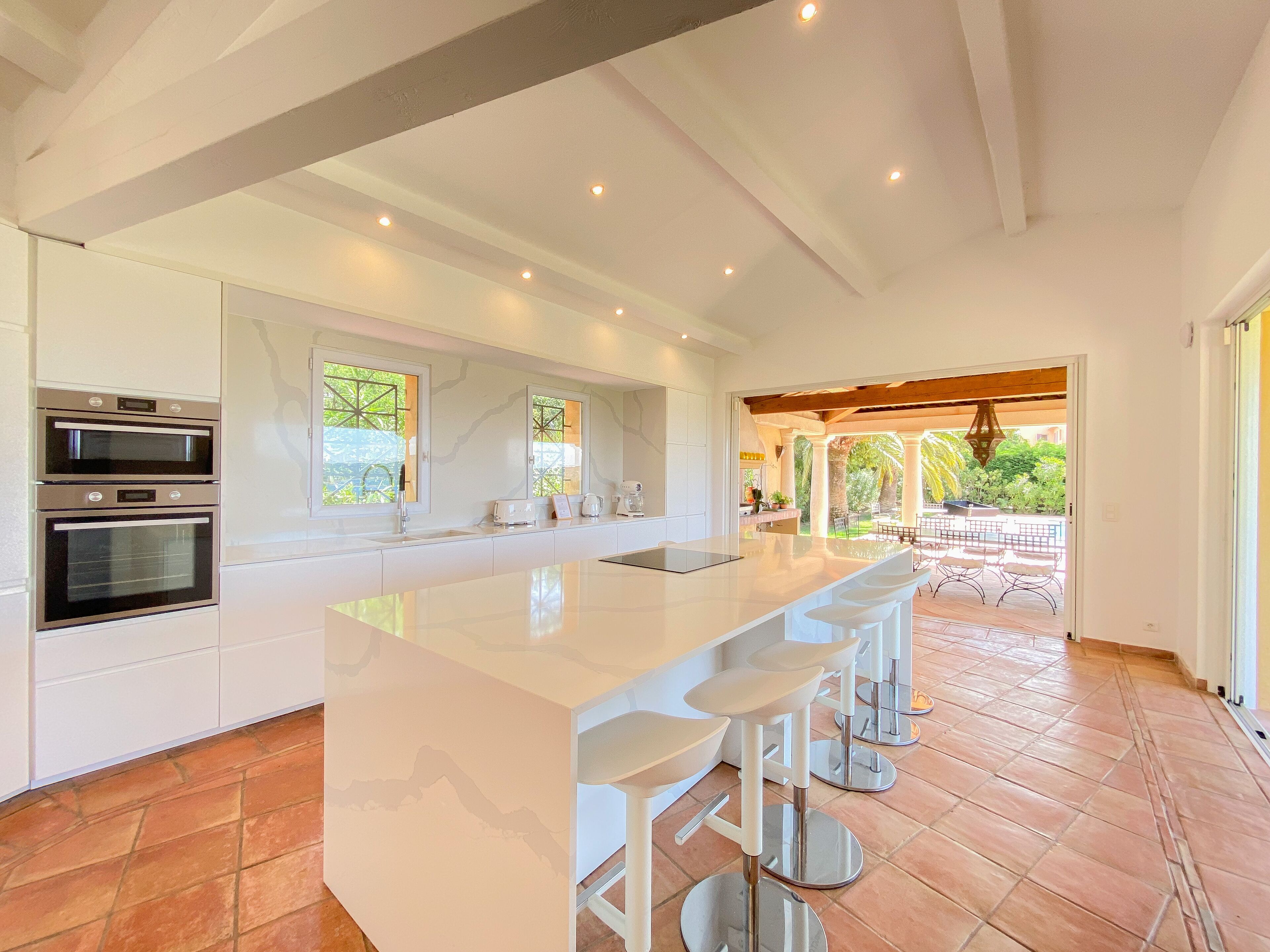 A modern kitchen with built-in ovens, a large island with bar stools, and a view of the outdoor patio area.