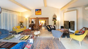 A spacious living room with a high ceiling, wooden beams, and a variety of seating options including a yellow armchair, a blue sofa, and a grey armchair. - Unique in Provence: the Mas Mirabelle in Eygalières (Eygalières)