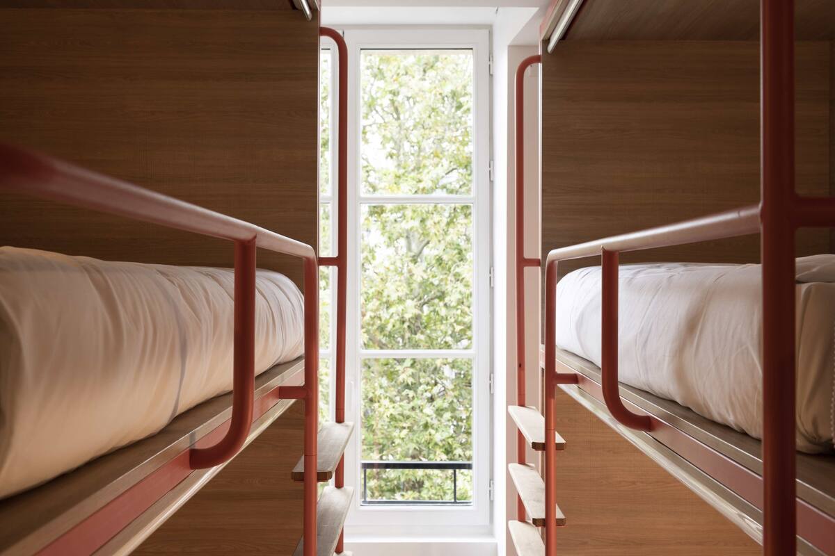 A bunk bed room with a window providing a view of trees.
