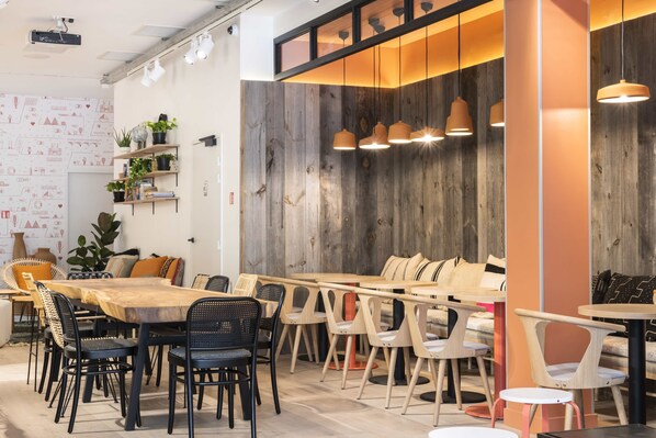 A modern cafe with a long wooden table, multiple chairs, and hanging pendant lights.