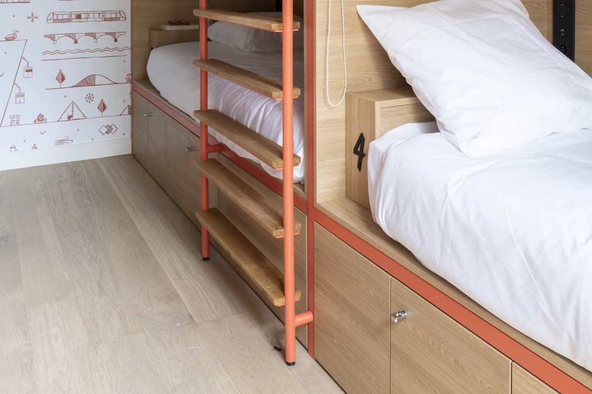 A bunk bed with a ladder, white bedding, and a wooden wall with a travel-themed wallpaper.