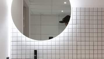 Un bagno moderno con uno specchio rotondo, un lavabo bianco e una parete rivestita di piastrelle.
