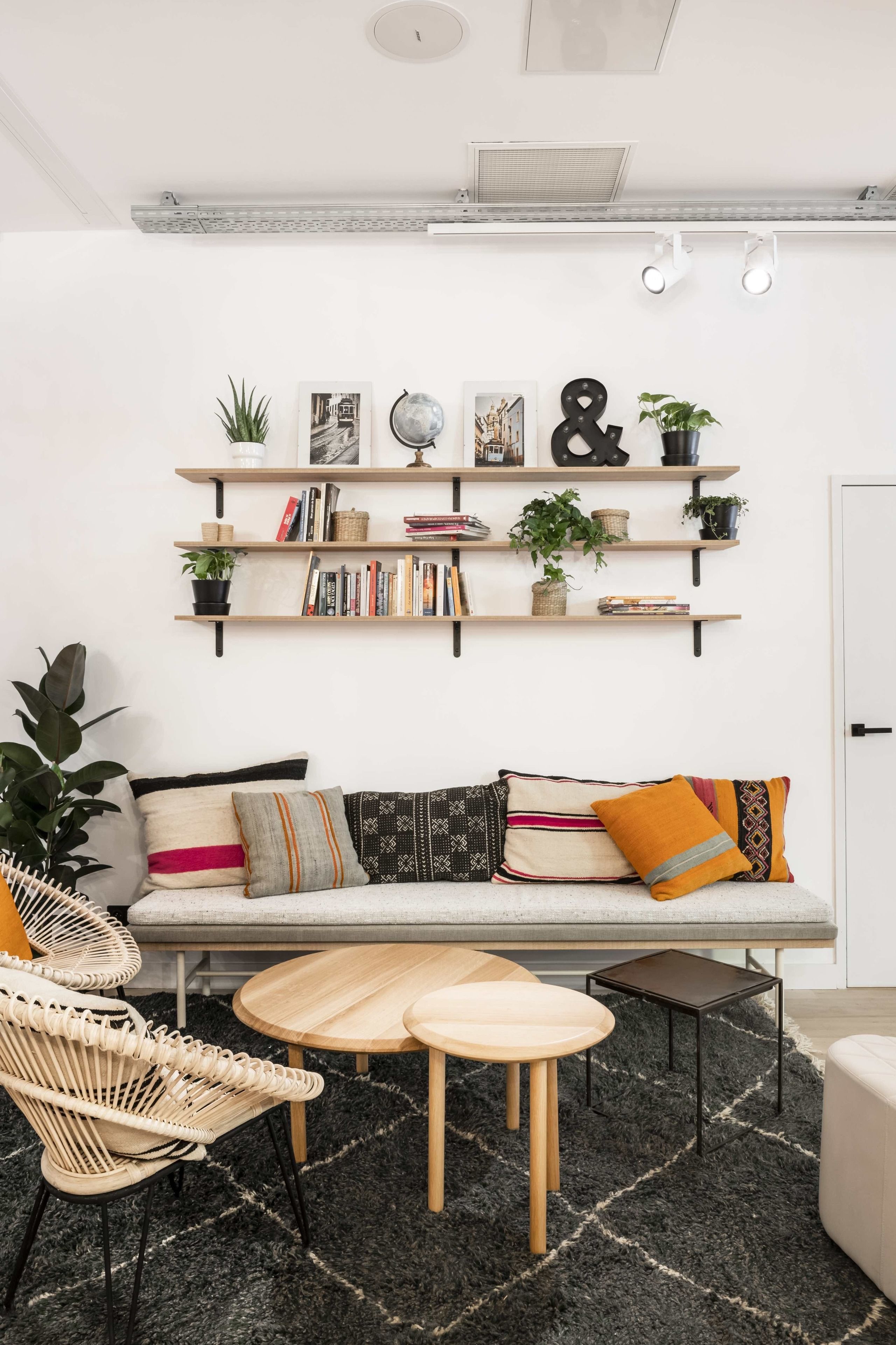 Un salon moderne comprenant un canapé, deux fauteuils, une table basse et une bibliothèque agrémentée de plantes et de livres.
