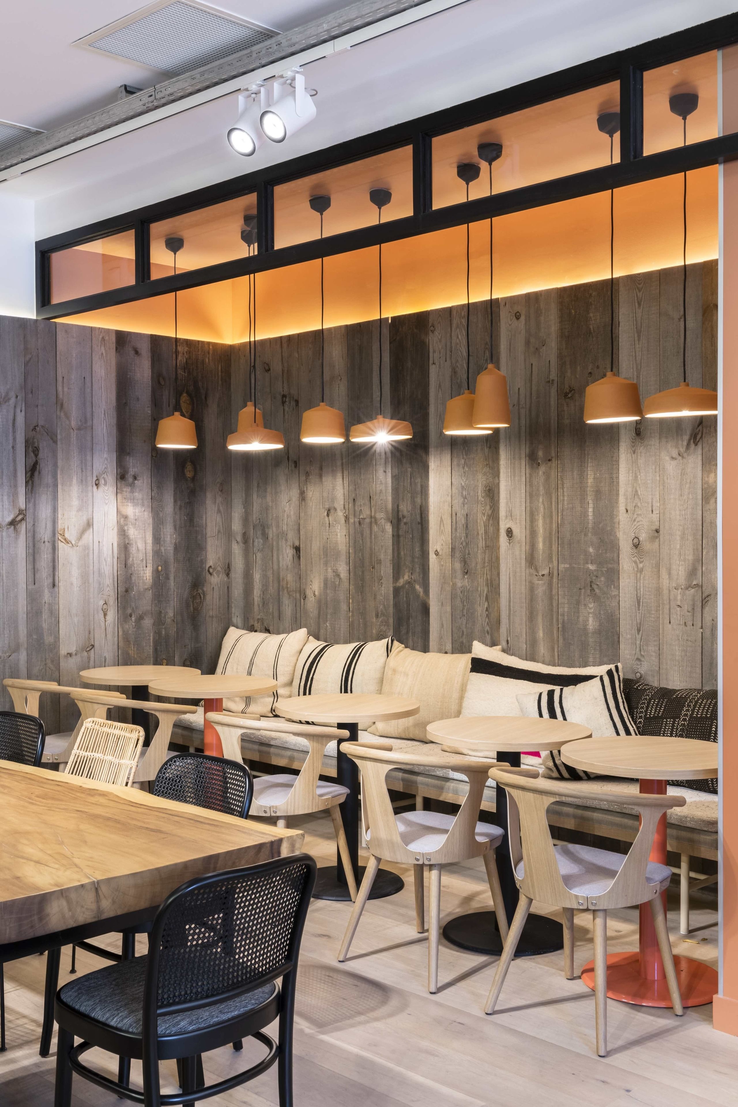 A modern dining area with a wooden wall, cushioned seating, and pendant lighting.