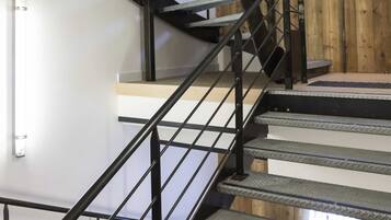 Una escalera de caracol con barandillas de metal y peldaños de madera, que conduce a un rellano con un muro de madera y un letrero de neón.