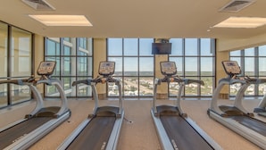 A gym with three treadmills, large windows, and a view of the city. - The Oasis at Orange Beach  - Lazy River + Slide, Pools, Splash Pad, Cafe & Bar.. (Orange Beach)
