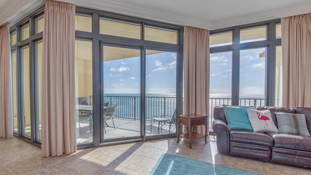 A spacious living room with a large sliding glass door leading to a balcony with a view of the sea. - The Oasis at Orange Beach  - Lazy River + Slide, Pools, Splash Pad, Cafe & Bar.. (Orange Beach)