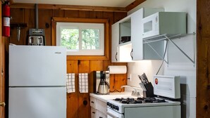 Eine kleine Küche mit Holzausstattung, einem weißen Kühlschrank, einem Herd und einer Mikrowelle.