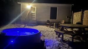 Eine Hütte mit Whirlpool, einer Holzterrasse und einer überdachten Veranda.