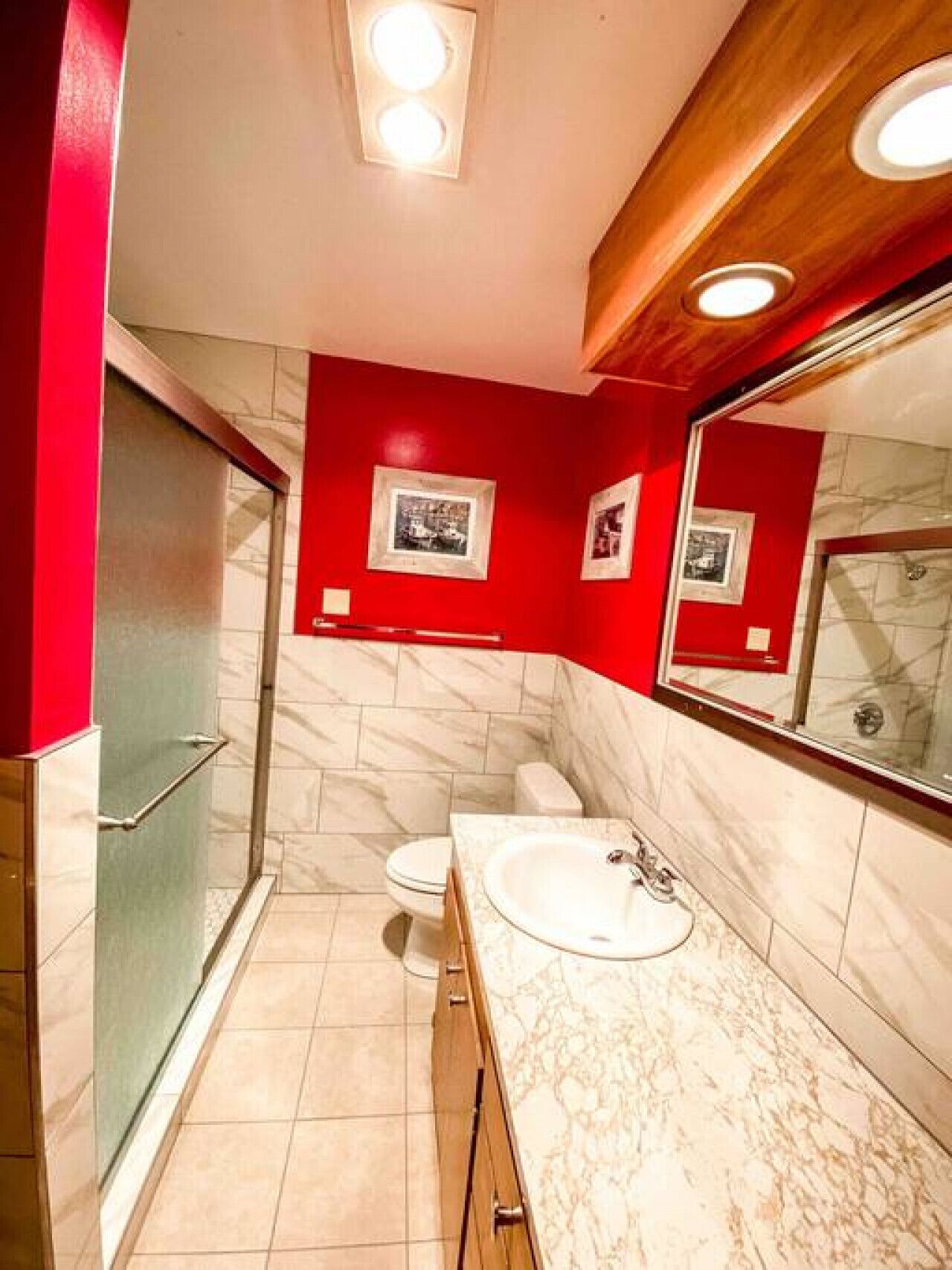 Une salle de bain moderne avec un mur d’accent rouge, un lavabo en marbre et une cabine de douche en verre.