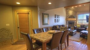 A dining area with a wooden table and chairs, a sofa, and a fireplace. - Smashing Location! - Affordable, Max. Amenities, Hot Tub, Views (Big Sky)