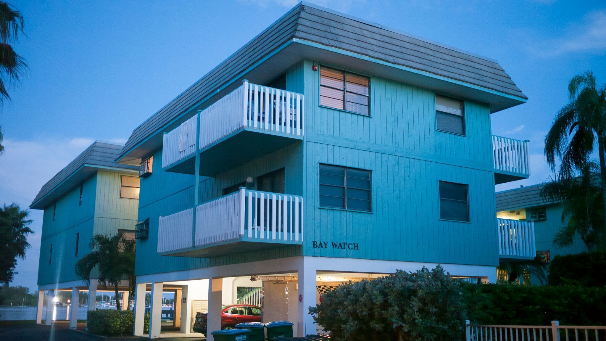 A two-story building with balconies, a garage, and a sign reading "BAY WATCH".