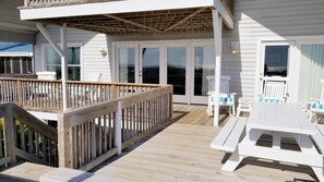 Une terrasse en bois avec une rambarde, des meubles d’extérieur blancs et un espace abrité agrémenté d’une pergola.