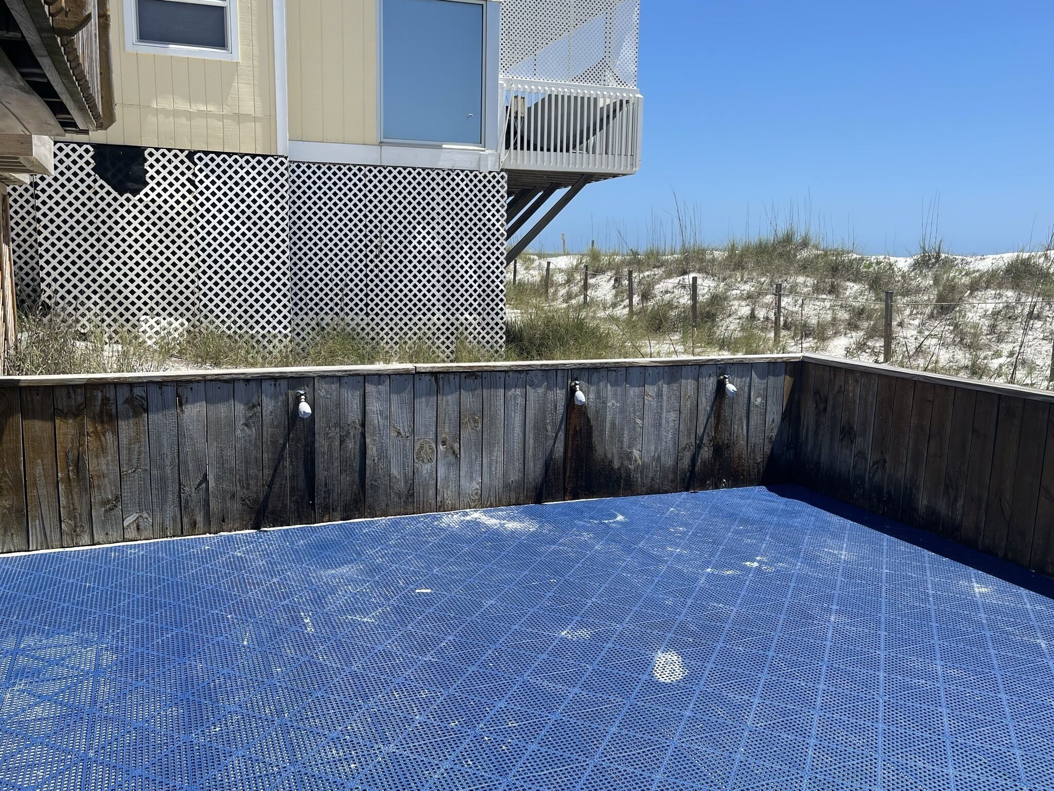 Une piscine dont le fond est bleu et présente une texture particulière, entourée d’une terrasse en bois et d’une clôture blanche à treillis.