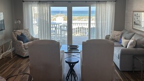 A living room with a view of the ocean, a balcony with outdoor furniture, and a dining area with two chairs and a table. - Pacifico Destin SPC 2135! An exquisite condo experience right on the beach! (Destin)
