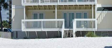 A two-story beachfront building with balconies, a sandy beach in front, and a clear sky.