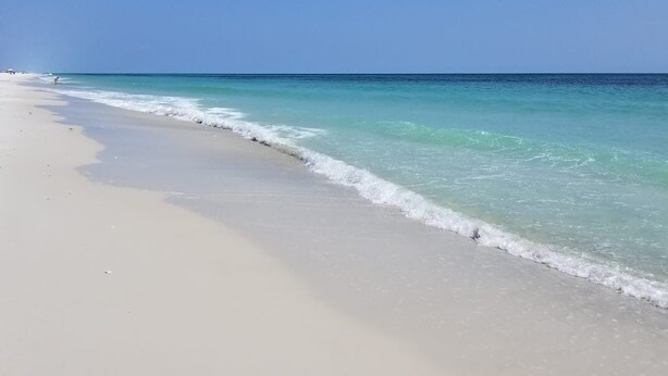 A beach with clear turquoise water and a wide sandy shore. - Pacifico Destin SPC 2135! An exquisite condo experience right on the beach! (Destin)