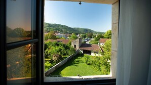 A view from a window overlooking a green courtyard with a stone wall, surrounded by buildings with red-tiled roofs. - La Maison de Siloe (Villefranche-de-Rouergue)