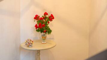Canto de um quarto com uma pequena mesa branca, um vaso de flores vermelhas e um objeto decorativo.