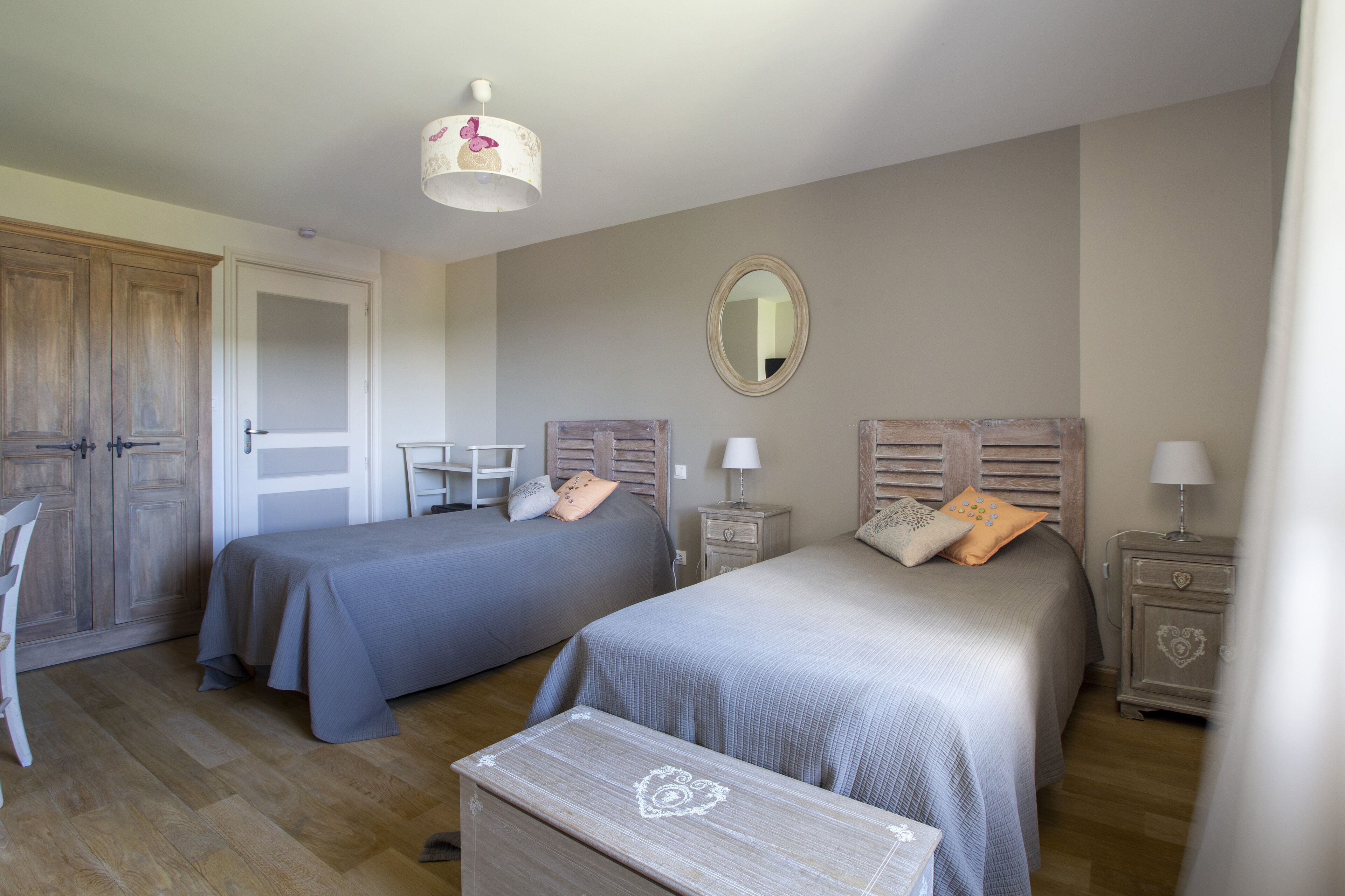 A bedroom with two beds, a wardrobe, a mirror, and a small table.