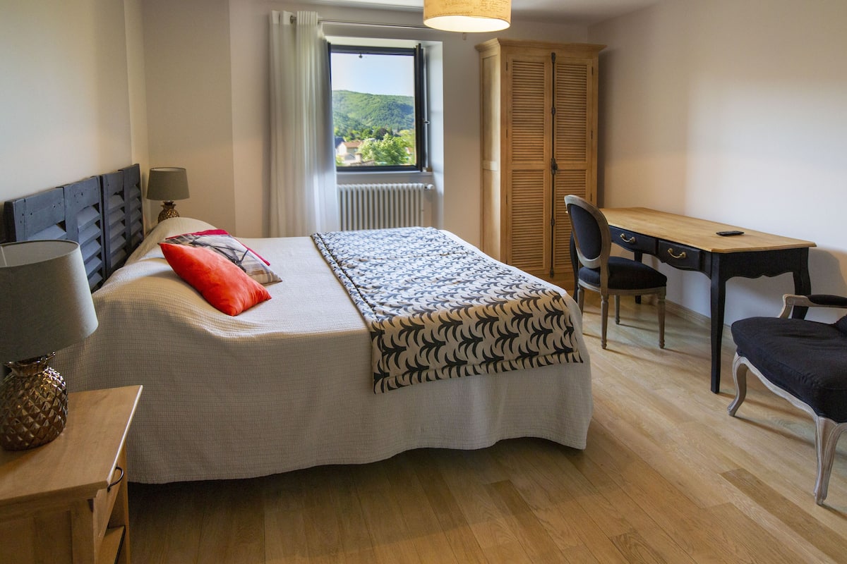 Ein Schlafzimmer mit Bett, Schreibtisch, Stuhl, Lampe und Blick ins Freie.