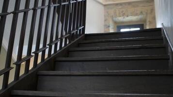 Una escalera de madera con barandilla de metal que lleva a un muro de piedra con una ventana.