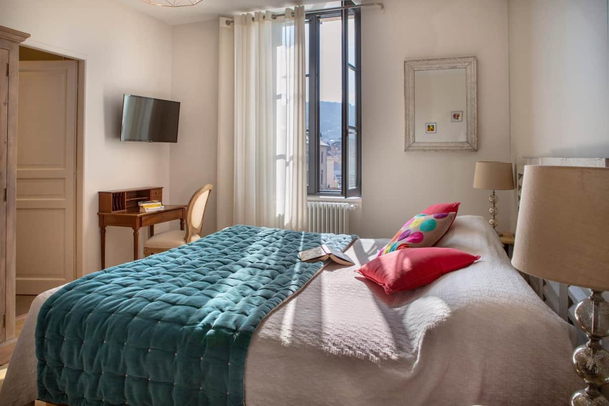 Ein Schlafzimmer mit Bett, Schreibtisch, Stuhl, Fernseher, Fenster und Heizkörper.
