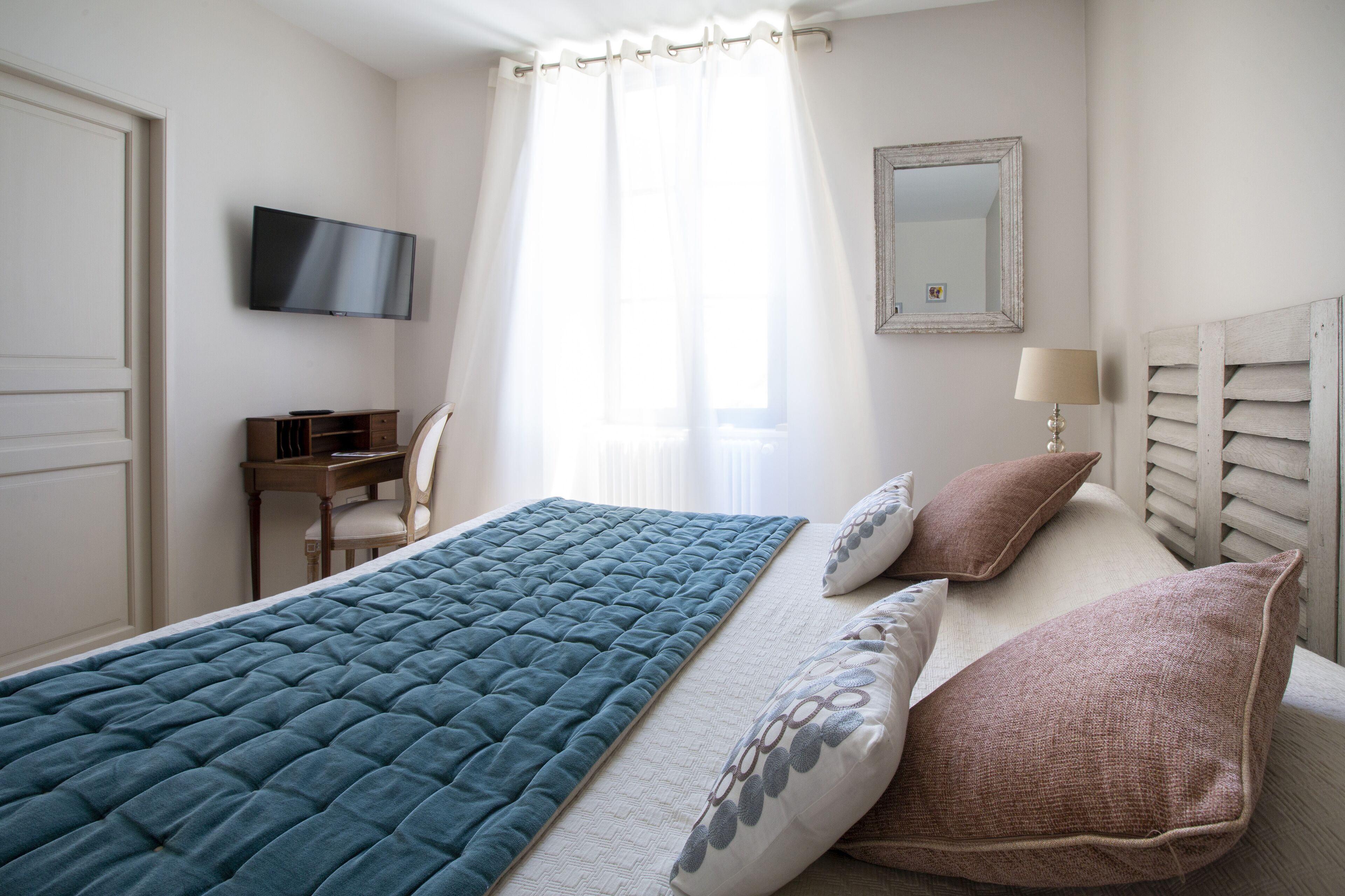 A bedroom with a bed, a desk, a chair, a television, a lamp, and a mirror.