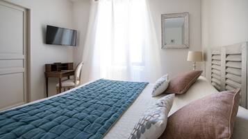 A bedroom with a bed, a desk, a chair, a television, a lamp, and a mirror.