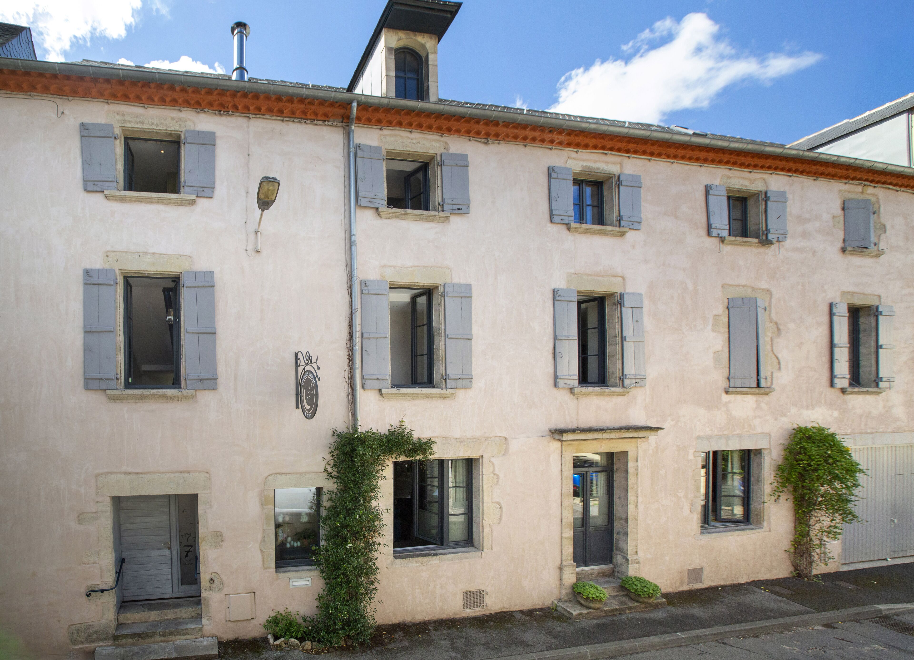 A building with multiple windows and doors, some with shutters, and a small garden area with plants.