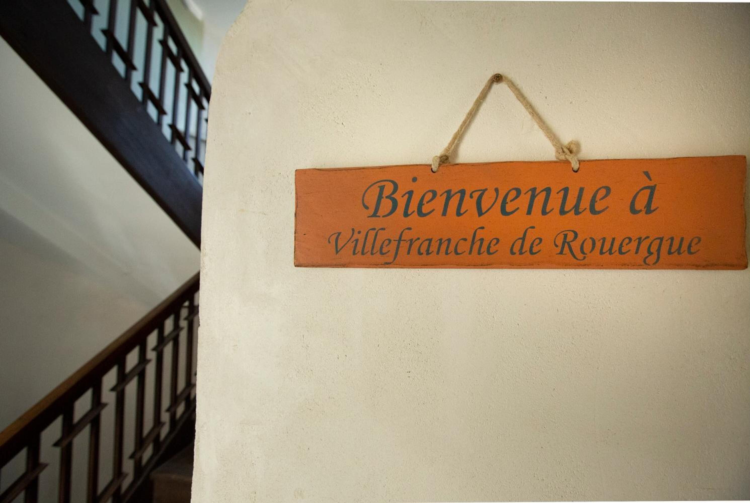 A welcome sign with the text "Bienvenue à Villefranche de Rouergue" hanging on a wall.