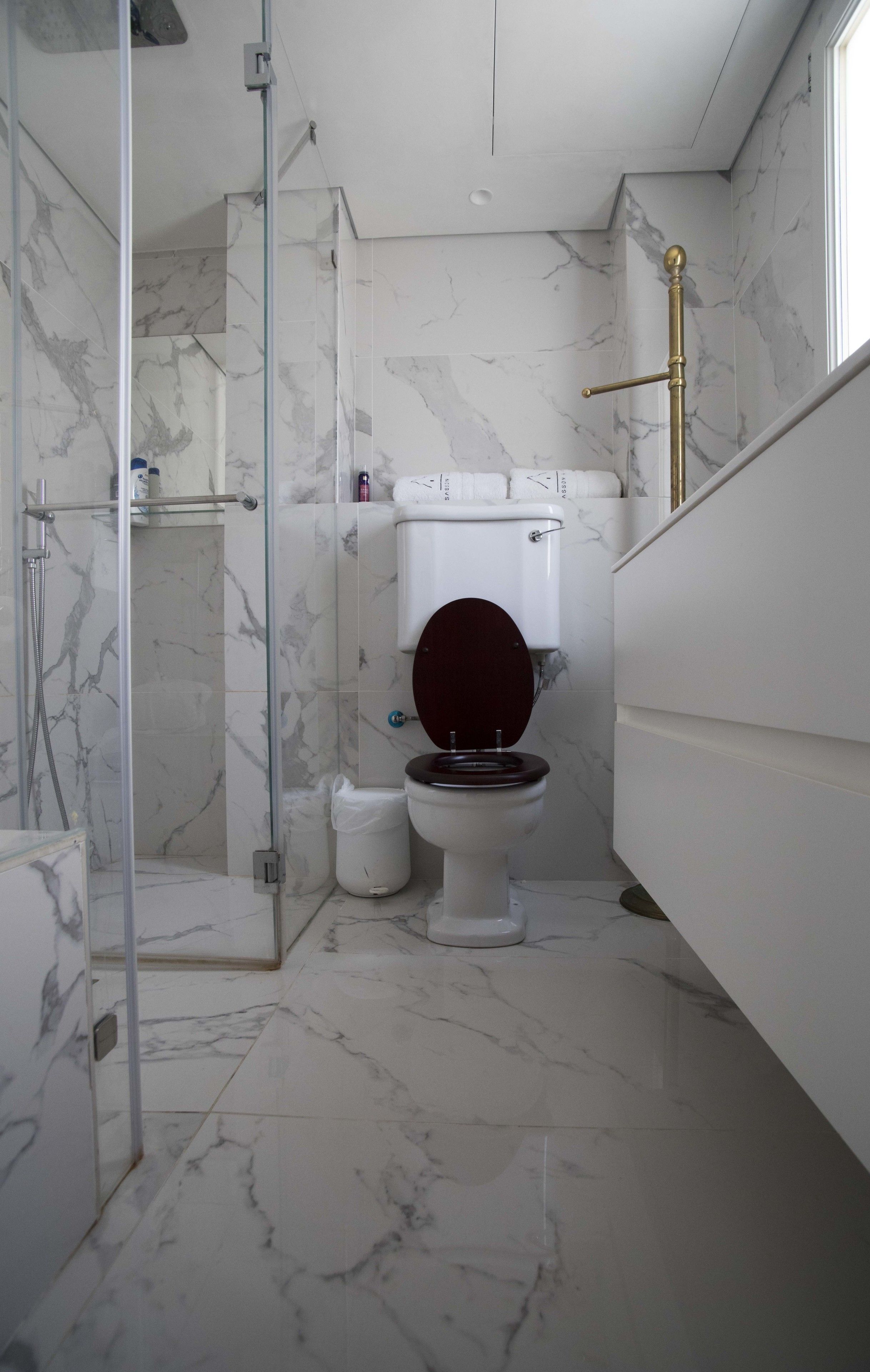 A bathroom with a toilet, shower, and marble flooring.