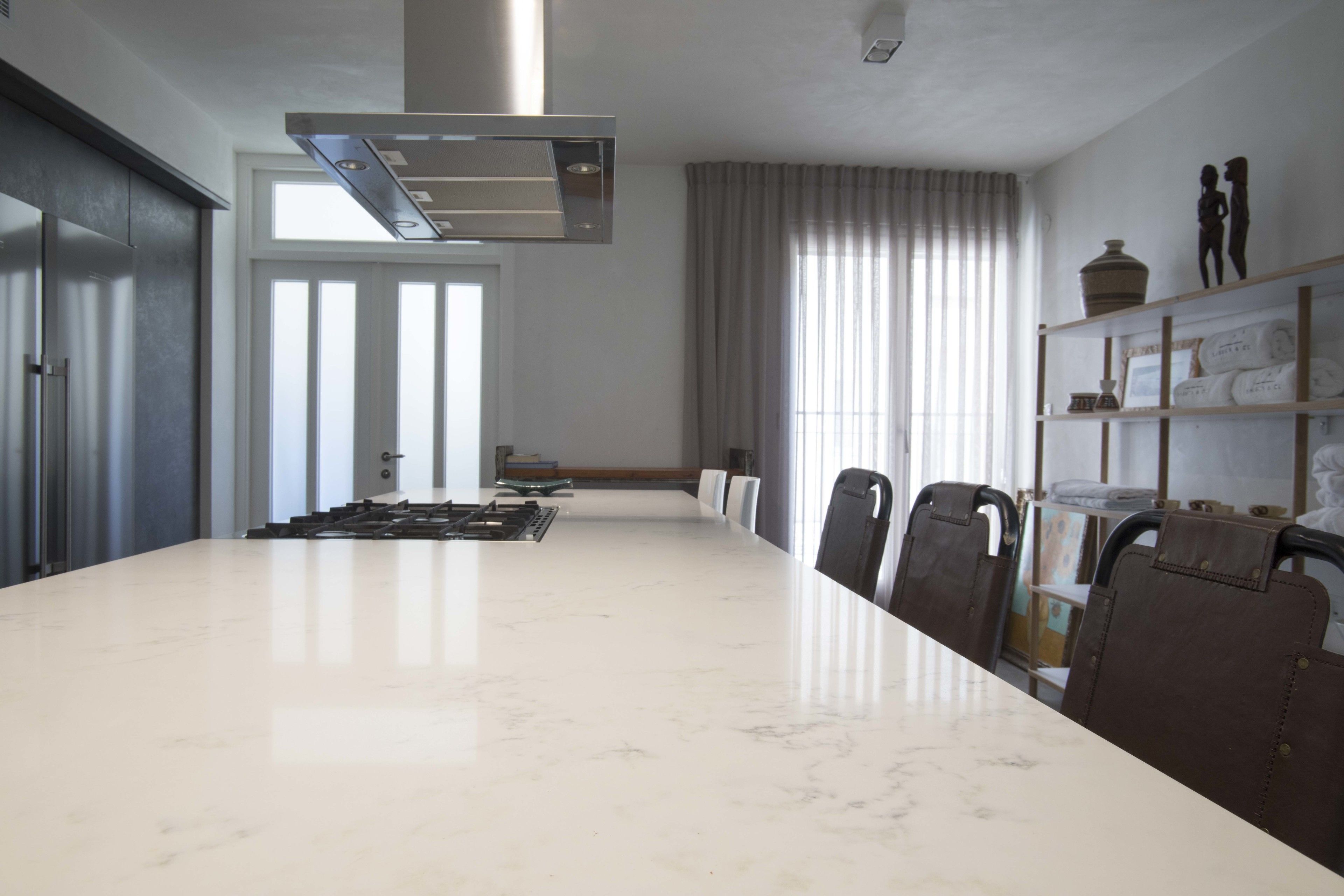 A spacious conference room with a large marble table, modern chairs, a built-in stove, and a large window with curtains.