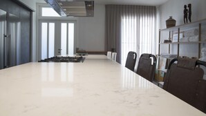 A spacious conference room with a large marble table, modern chairs, a built-in stove, and a large window with curtains. - Sasson & Co Luxury apartment Neve Tsedek (Tel Aviv)