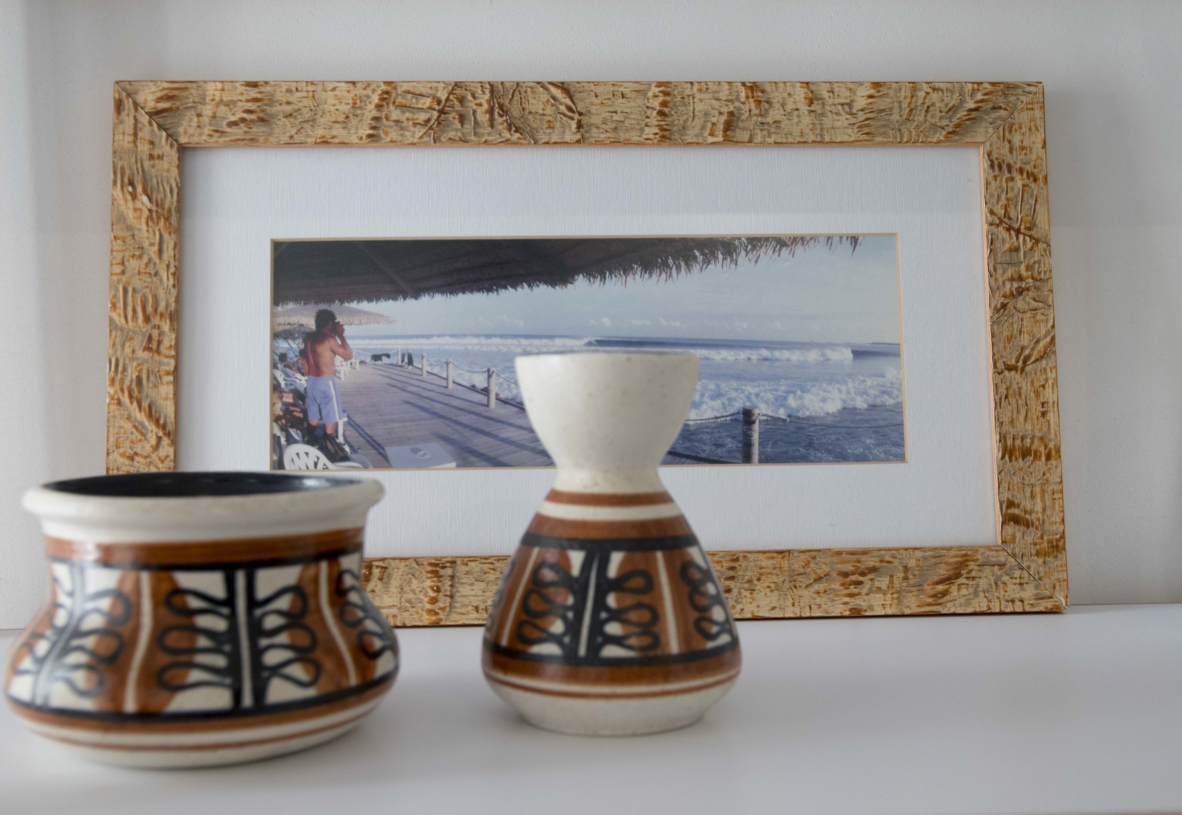 A framed photograph of a beach scene with a person in the water, two decorative vases, and a wooden-framed picture.