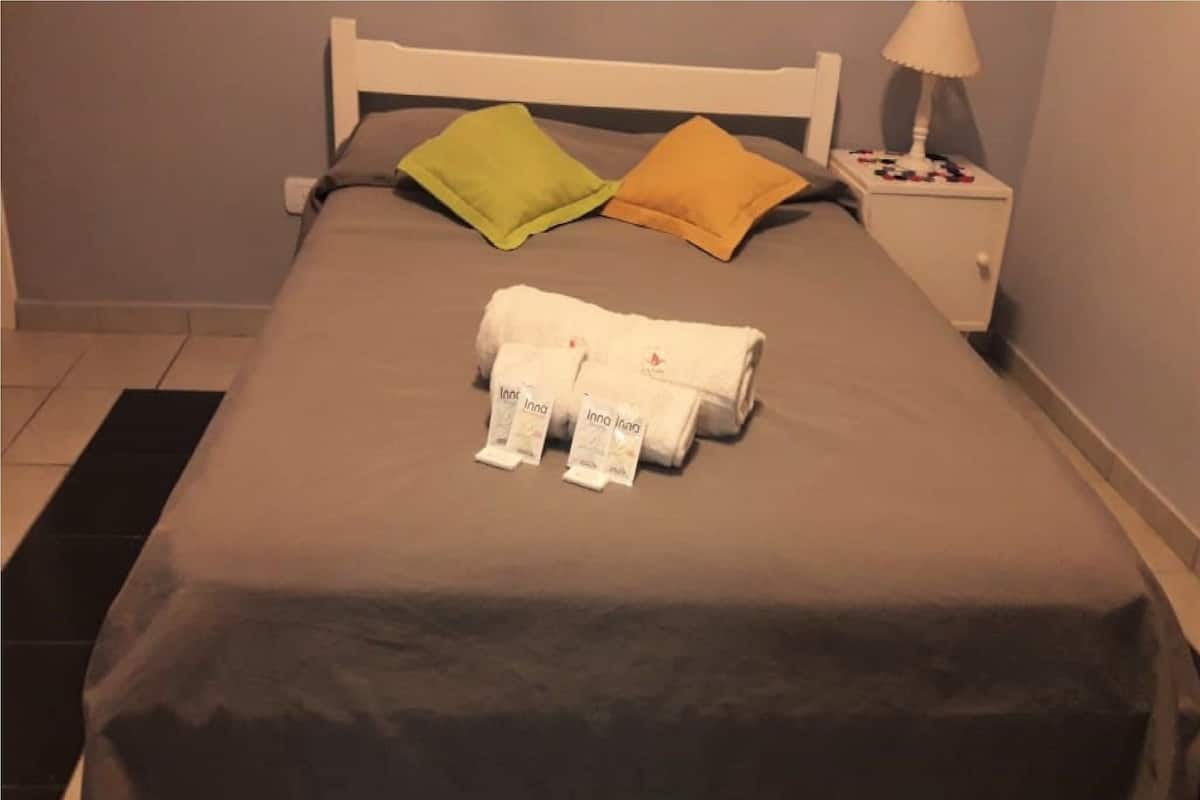 Una cama bien hecha con una colcha gris, dos almohadas y un juego de toallas dobladas sobre la cama.