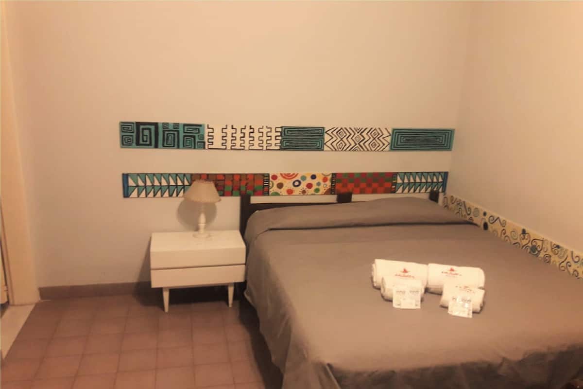 Una habitación de hotel con una cama, una mesita de noche con lámpara y un cabecero con diseños estampados.