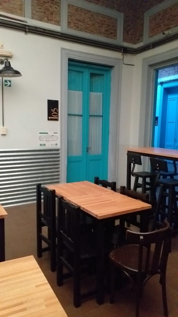 Una habitación con una mesa y sillas de madera, una puerta azul y un letrero con un número en la pared.