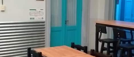Una habitación con una mesa y sillas de madera, una puerta azul y un letrero con un número en la pared.