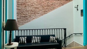 A room with a brick wall, a black sofa with striped pillows, a small white table with a lamp, and a blue door with the number 101. - Hotel La Barca (Buenos Aires)