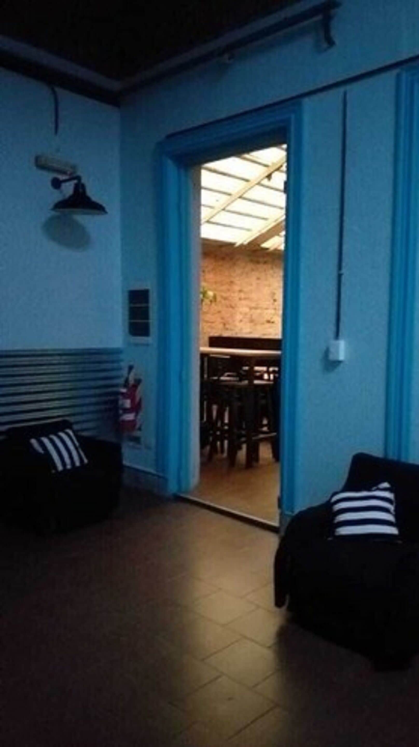 A room with a blue door leading to a dining area, a ceiling fan, and a fire extinguisher on the wall.