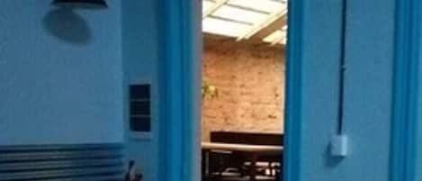 Una habitación con una puerta azul que da a un comedor, un ventilador de techo y un extintor en la pared.
