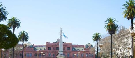 A large building with a central statue, surrounded by palm trees and street lamps.