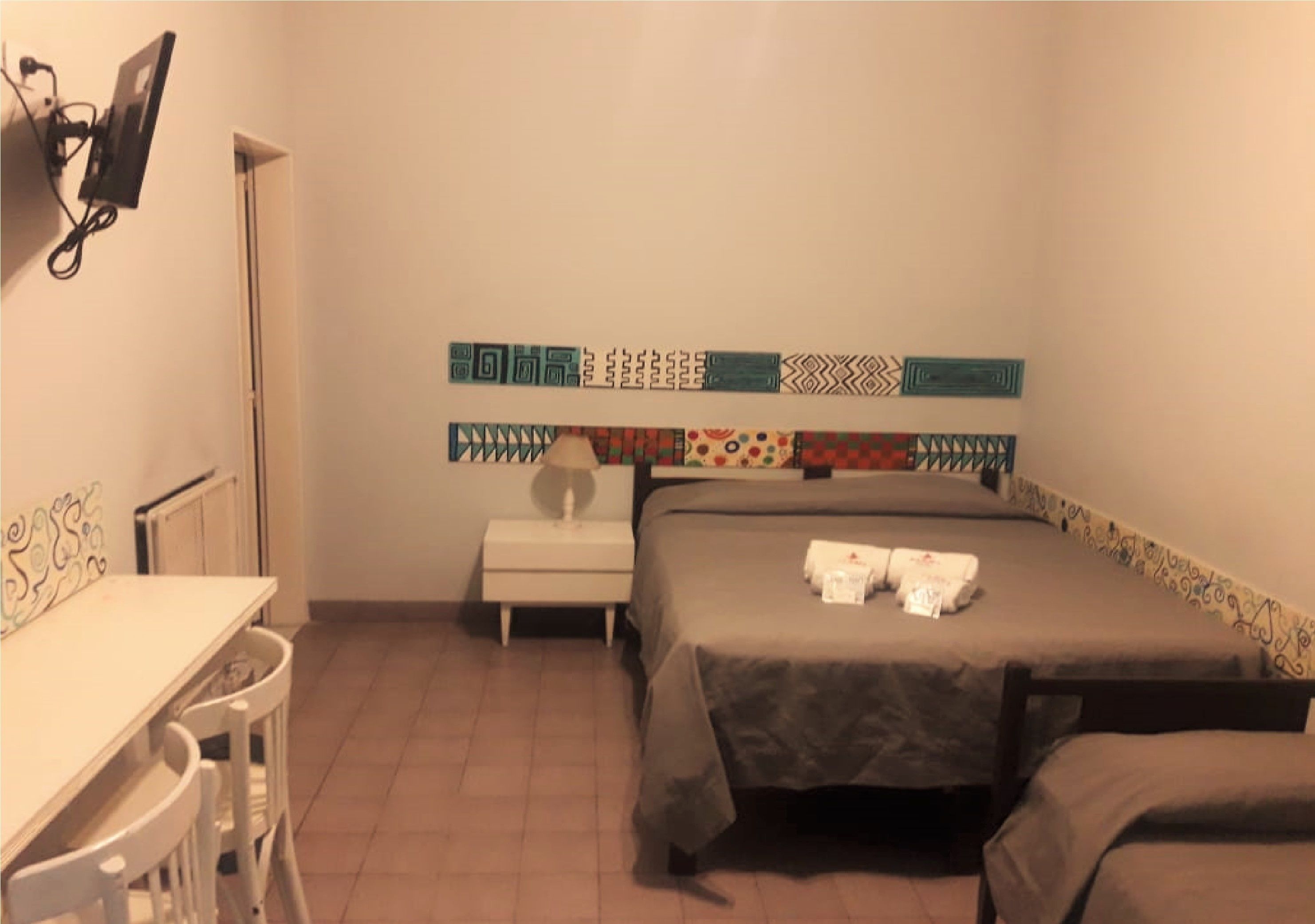 A bedroom with two beds, a small bedside table, a chair, and a desk.