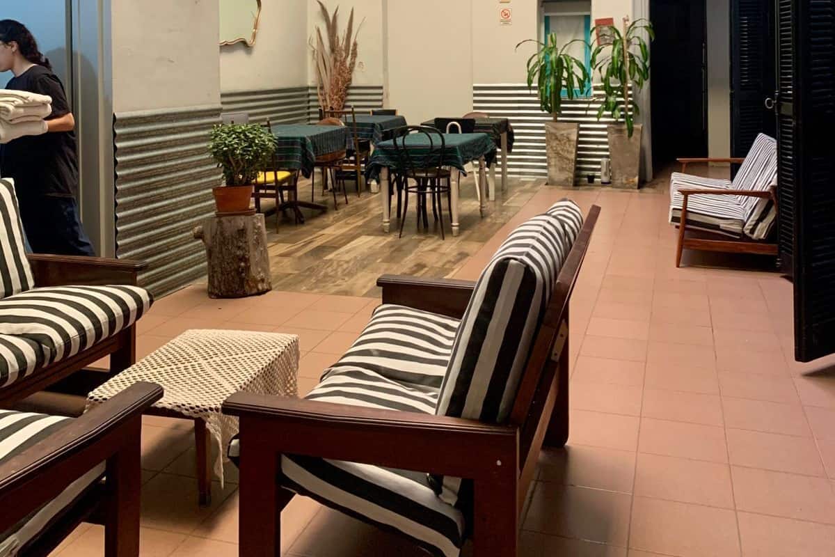 Un espacio interior amplio con techo alto, que incluye una zona de estar con sofás y sillones a rayas, una zona de comedor con mesas y sillas, y una escalera que conduce a un nivel superior.