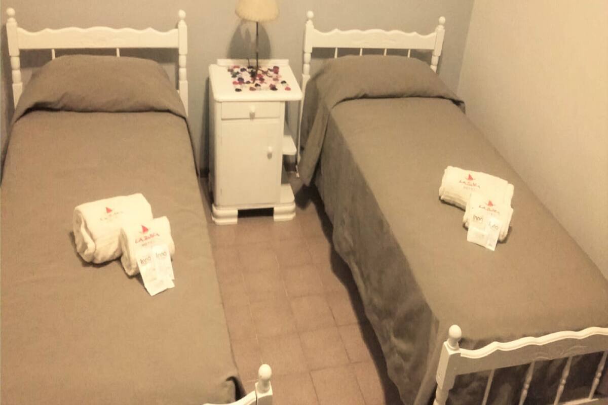 Habitación doble con dos camas, una mesita de noche y una lámpara.