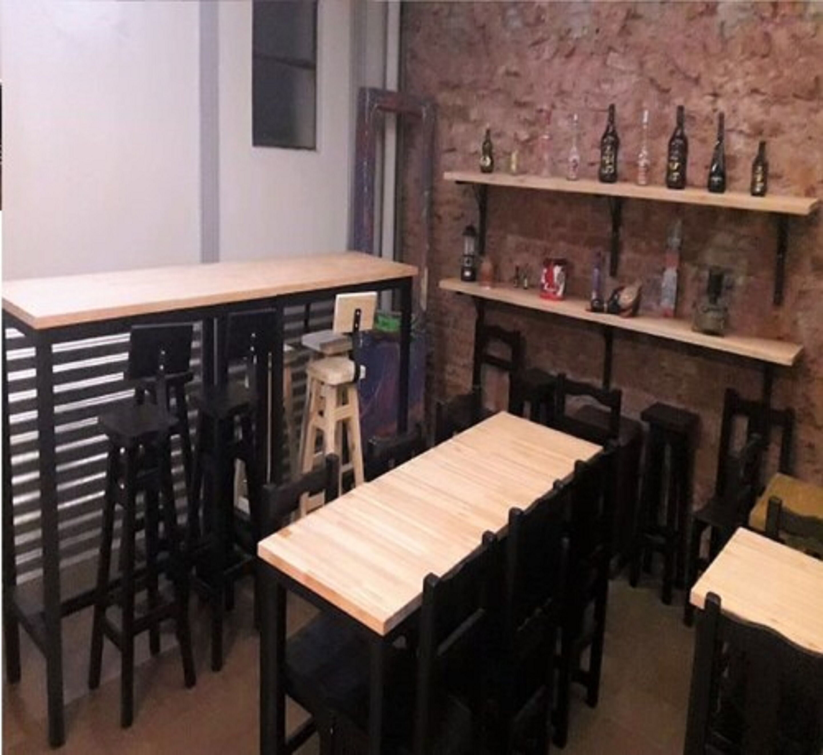 A restaurant with wooden tables and chairs, a brick wall, and shelves with bottles.