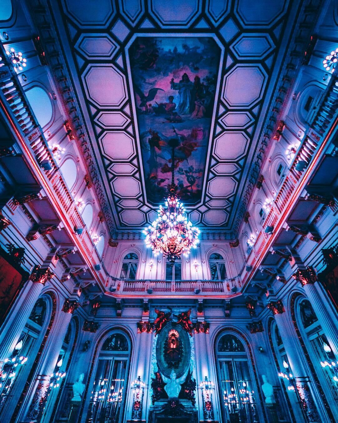 A grand hall with a large chandelier, ornate ceiling, and classical architecture.