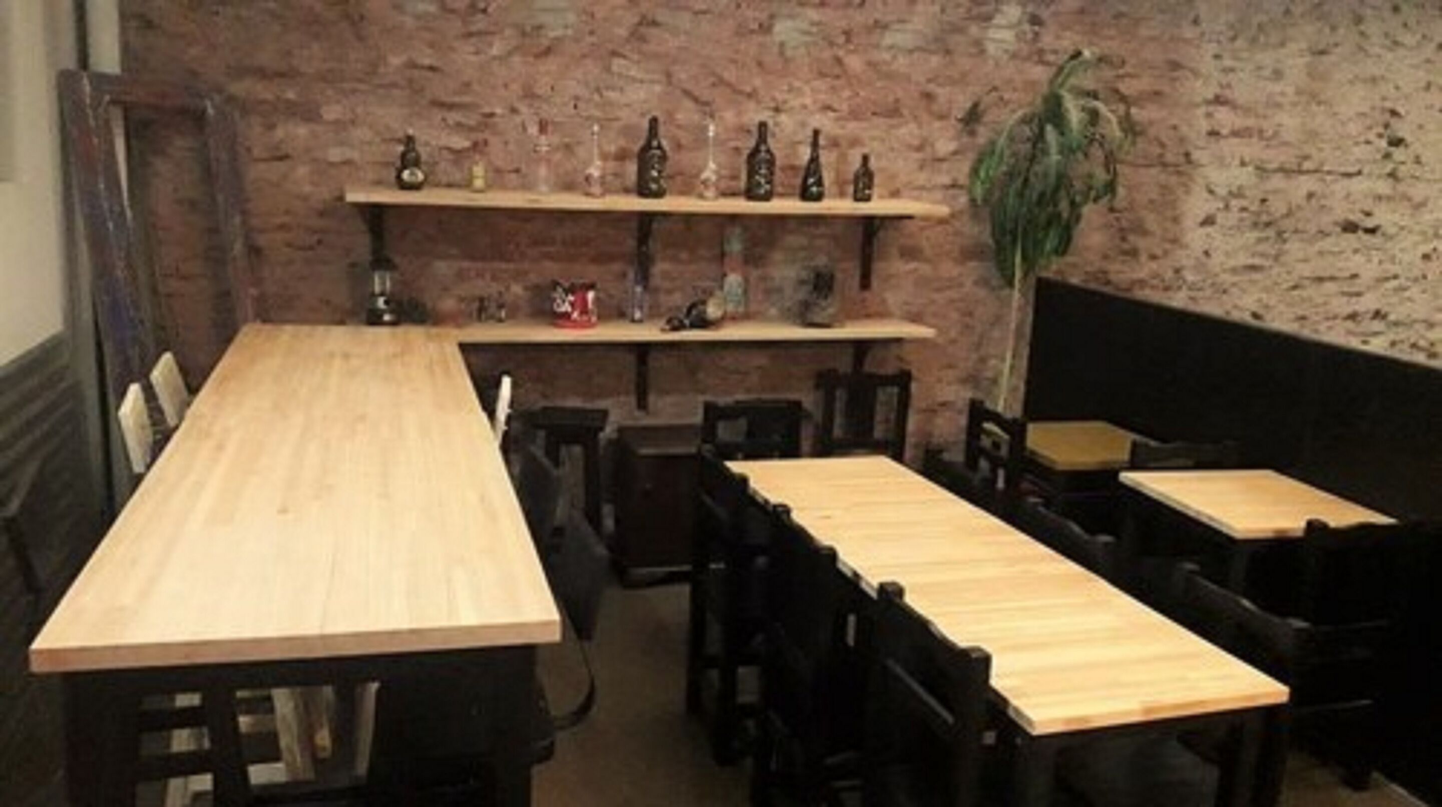 Interior de restaurant amb taules i cadires de fusta, una paret de maó i prestatges amb ampolles.