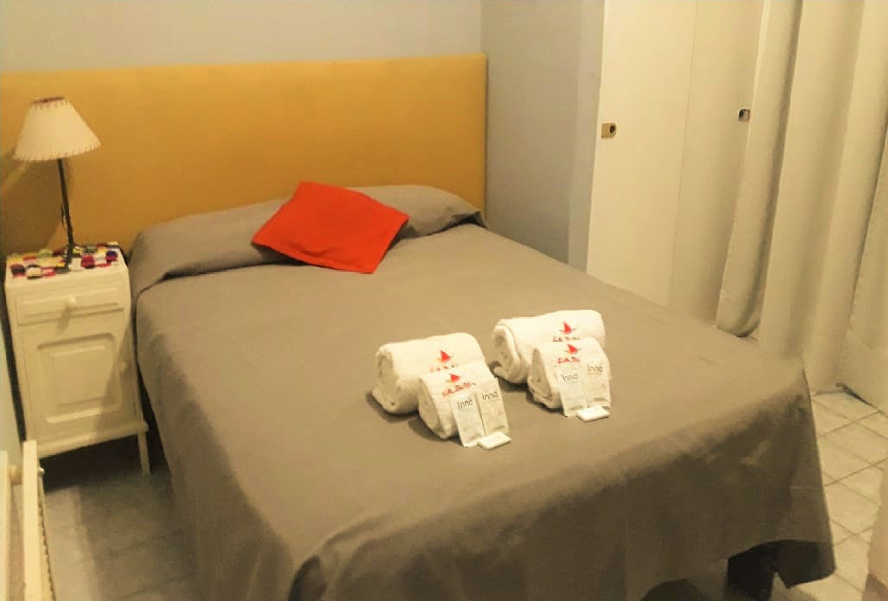 A hotel room with a bed, a nightstand, a lamp, and towels on the bed.